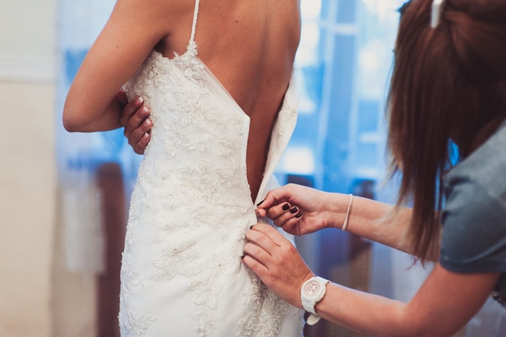 woman zipping bride's wedding dress