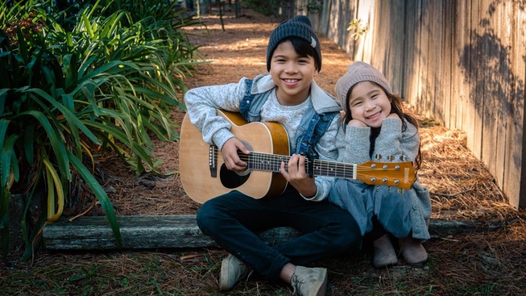 kids sitting and smiling holding a guitar