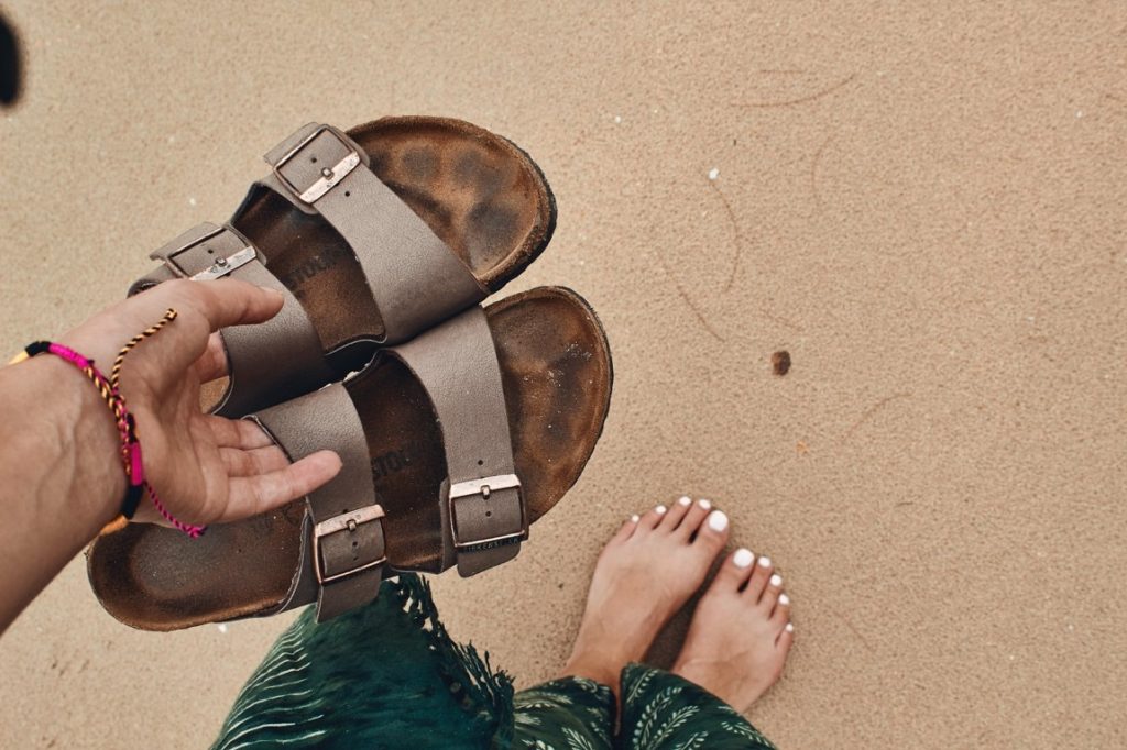 barefoot girl holding her slippers at the beach