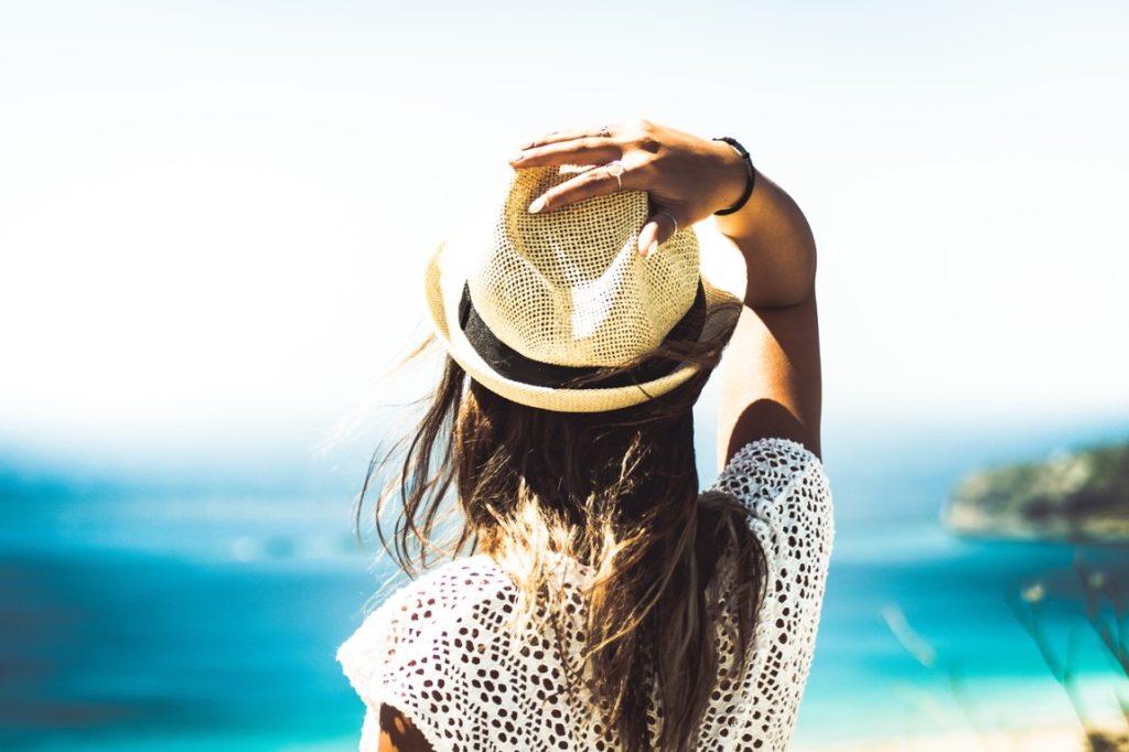 woman on a beach keeping her hat intact