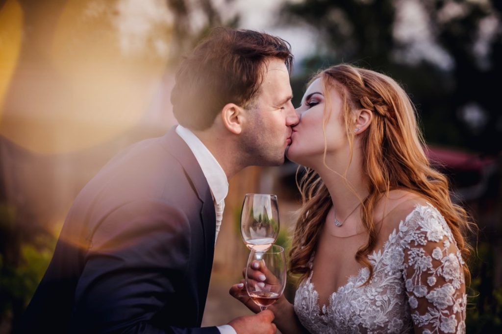 bride and groom kissing while holding wine glass