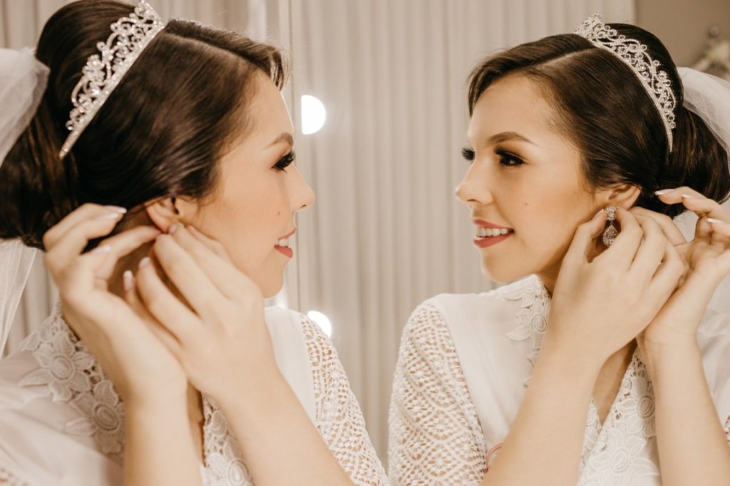 bride putting earrings on while looking in the mirror
