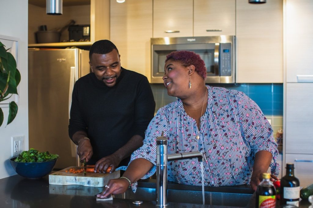 man chopping carrots while woman cleans kitchen