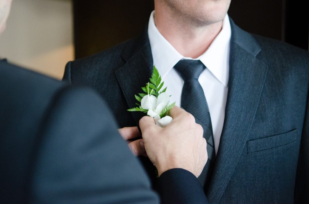 man putting a boutonniere on his friend's suit