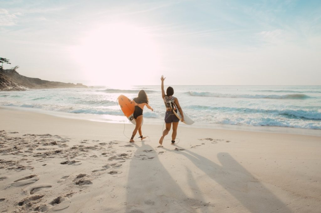 two woman carrying surfing board near the sea