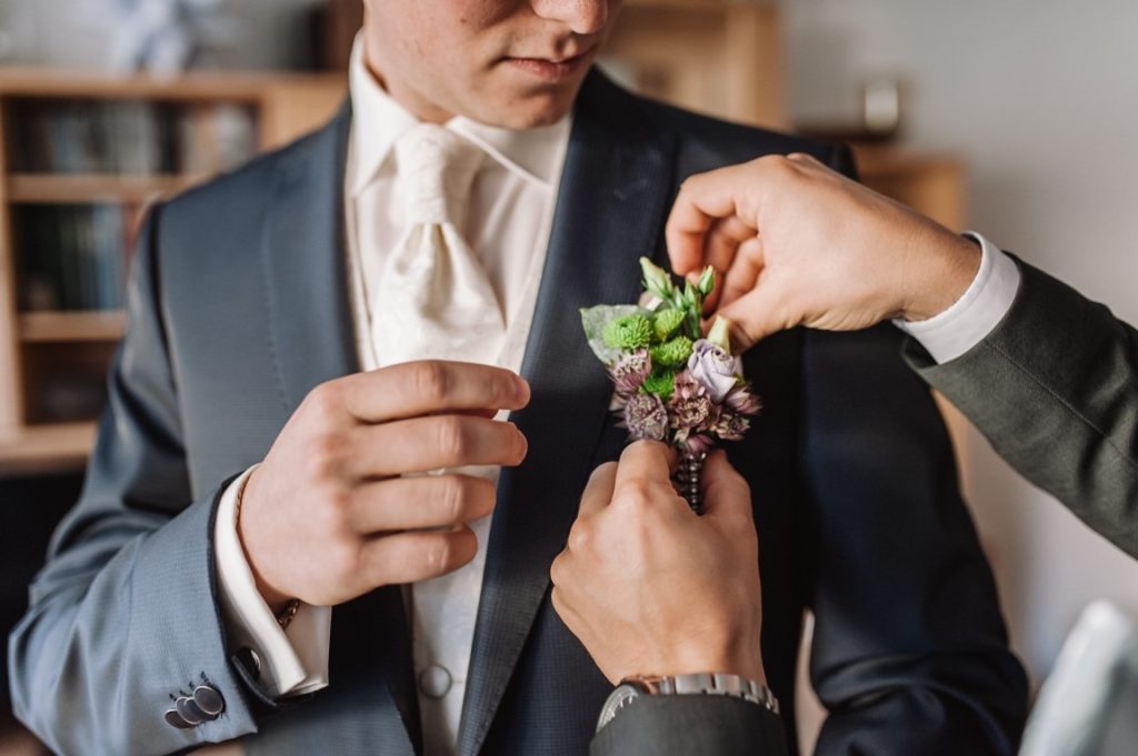 man putting a corsage on another man's suit