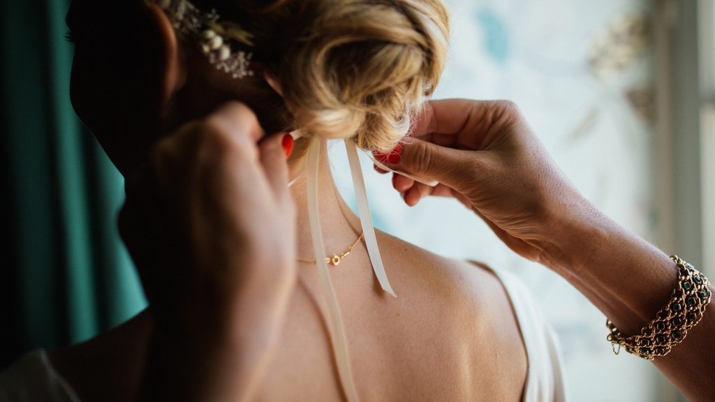 woman fixing ribbon on bride hair