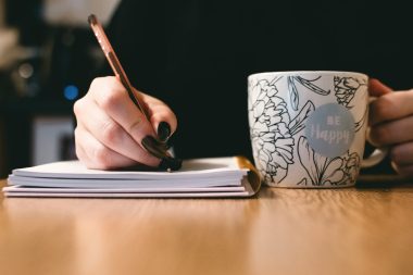 woman writing while holding a ceramic mug
