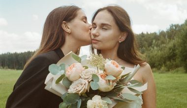 woman kissing a woman while holding a flower