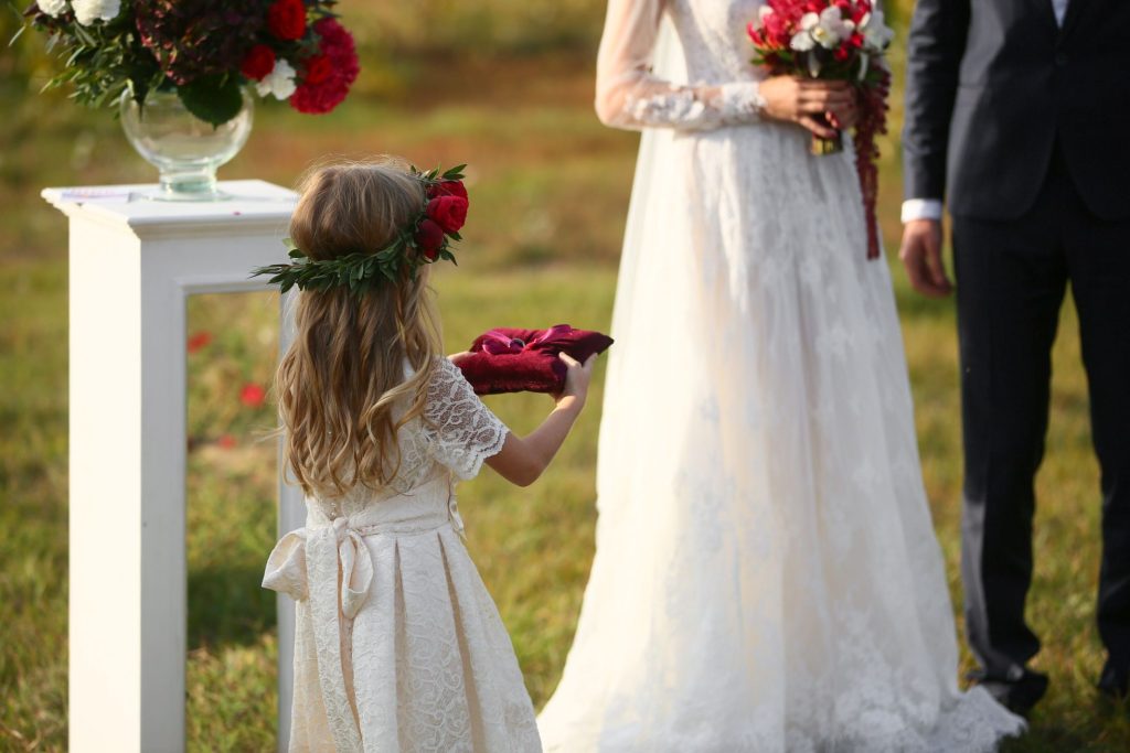 a little girl presenting a wedding ring on a cushion to a couple