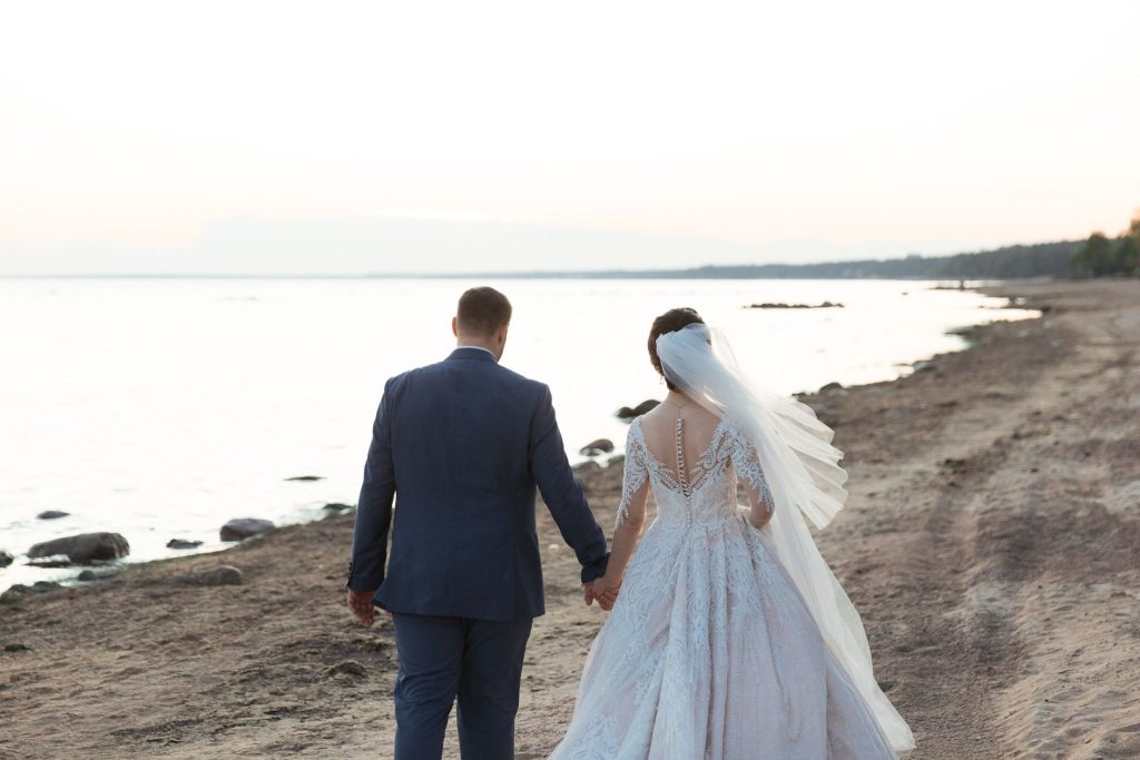 bride and groom in wedding attire on the beach looking at the sea