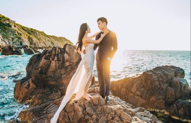 man and woman standing on a rock on the sea