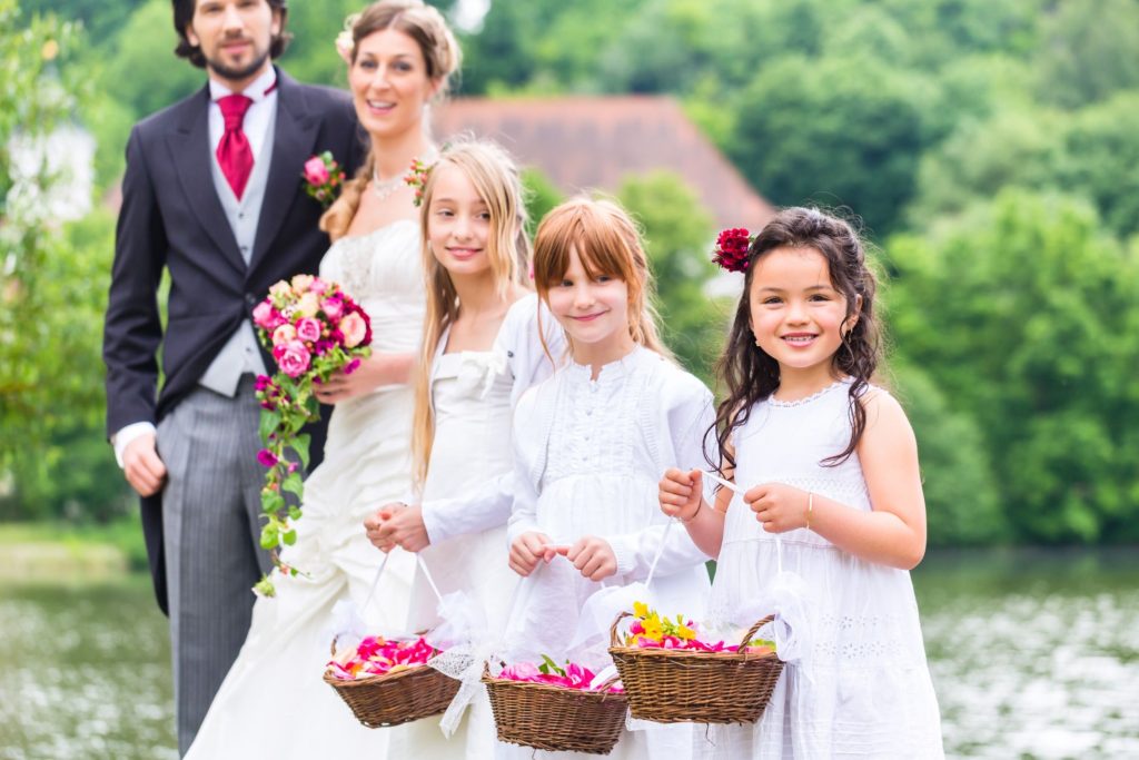 three flower girls wearing white dresses standing in front of a newly married couple