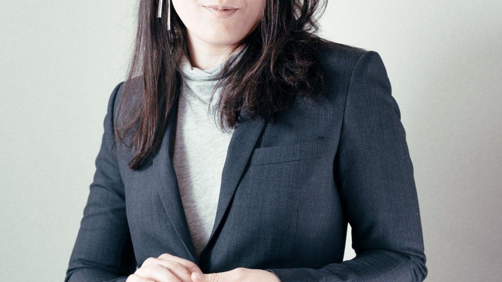 woman wearing a light gray turtleneck under a dark gray blazer