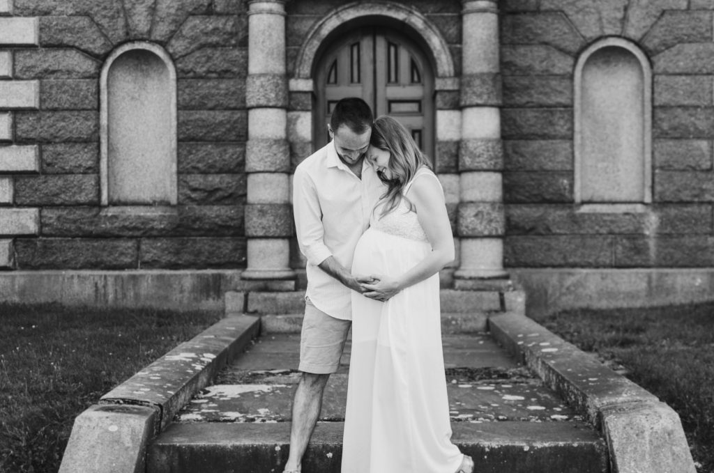 a couple in wedding attire embracing while fondly looking at the woman's baby bump