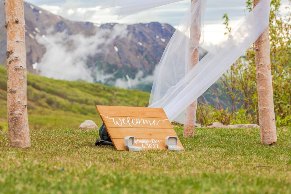 a welcome signage for a wedding sits on grass with a mountain in the backdrop