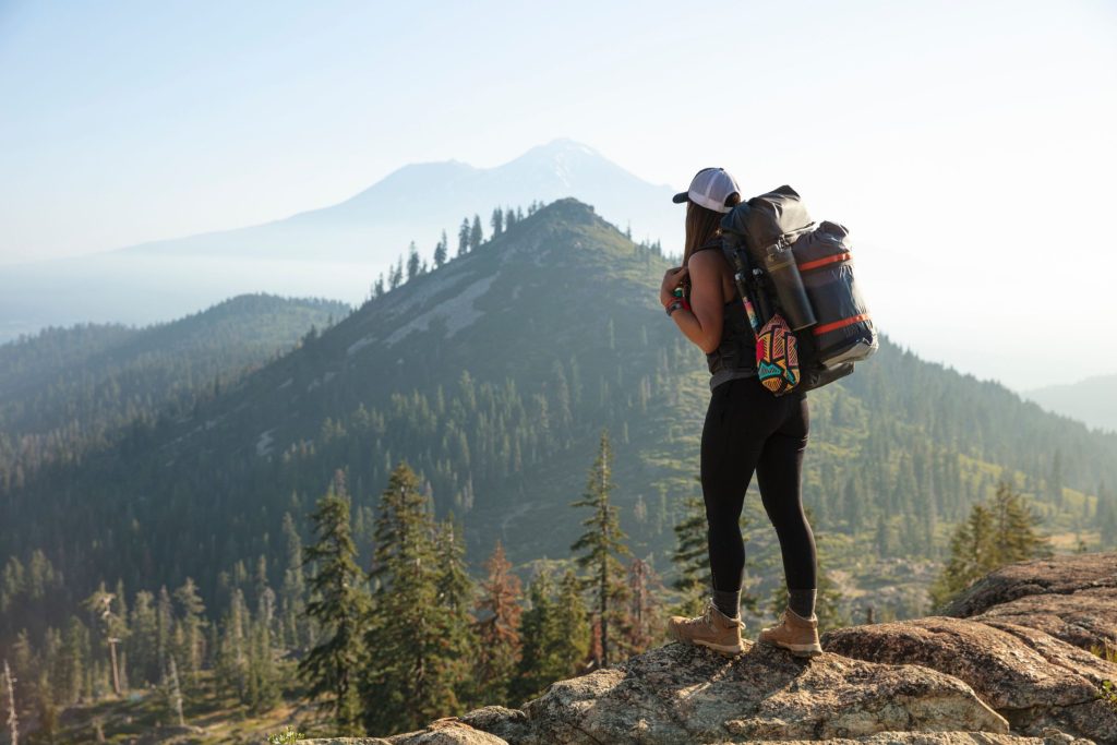 a woman carrying a large backpack standing on a rock looking onto a mountain
