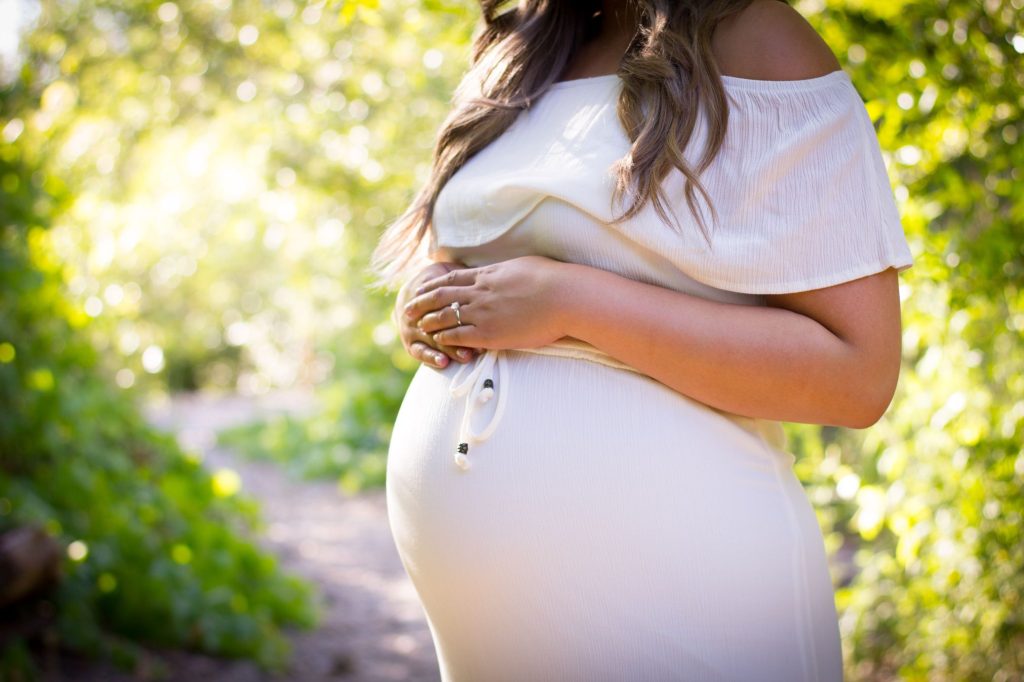 a woman wearing a white blouse and skirt showing off her engagement ring and baby bump