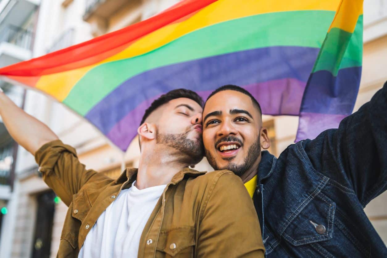 two gay men kissing and holding up a pride flag