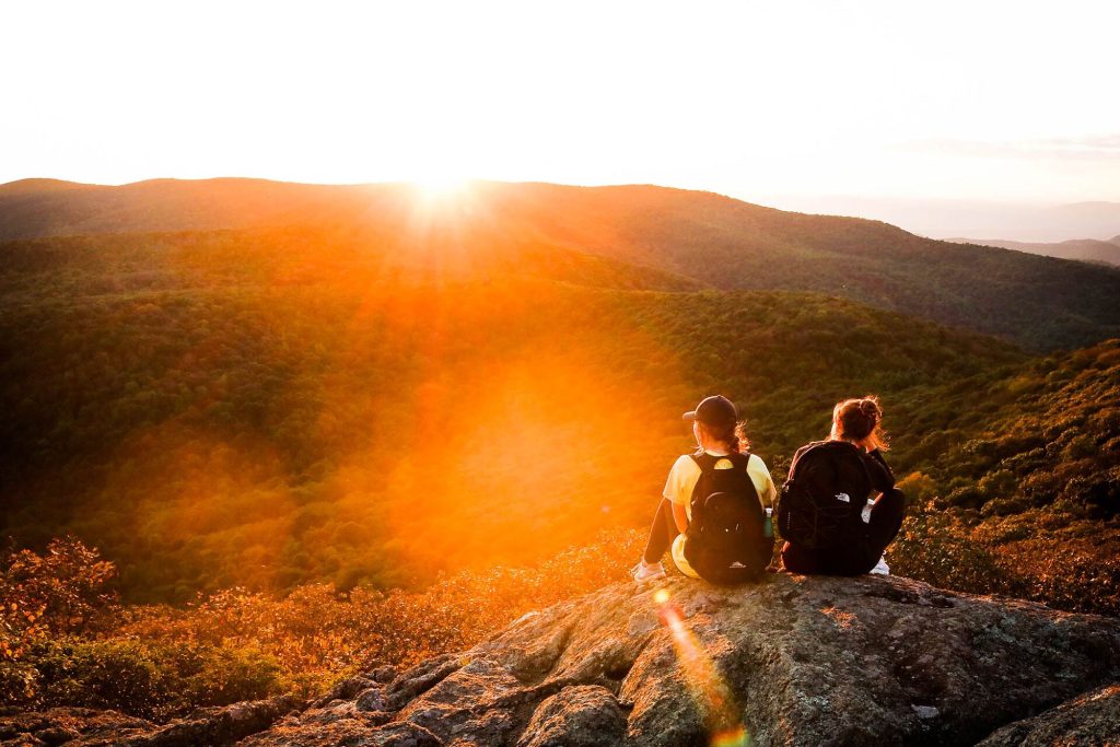 two women sitting on a rock on a mountain as they watch the sunset