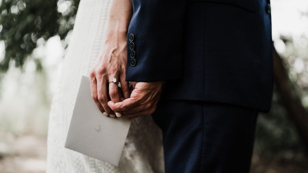 envelope tucked within bride and groom's intertwined hands