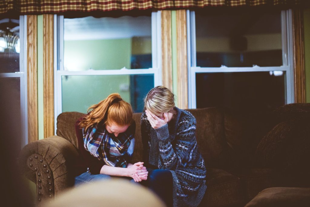 two women sitting holding hands as they look down sadly