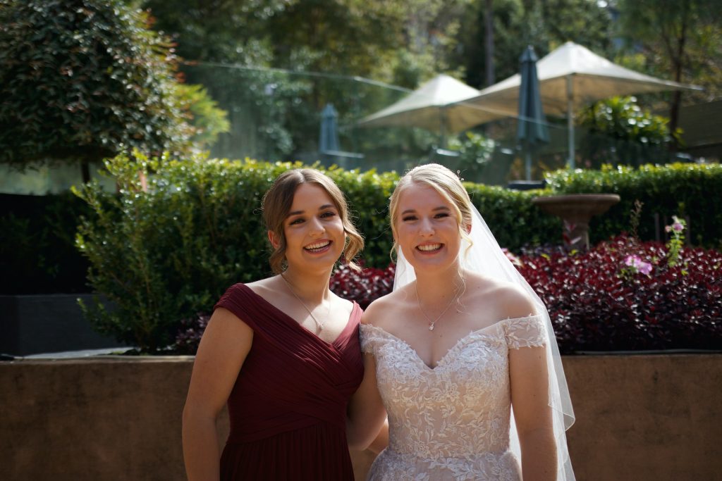 bride and bridesmaid posing for a photo in front of greenery