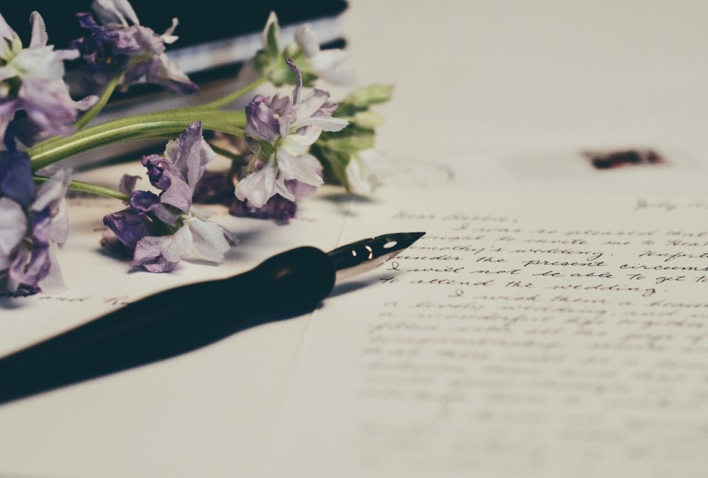 fountain pen and purple flowers on top of a handwritten letter