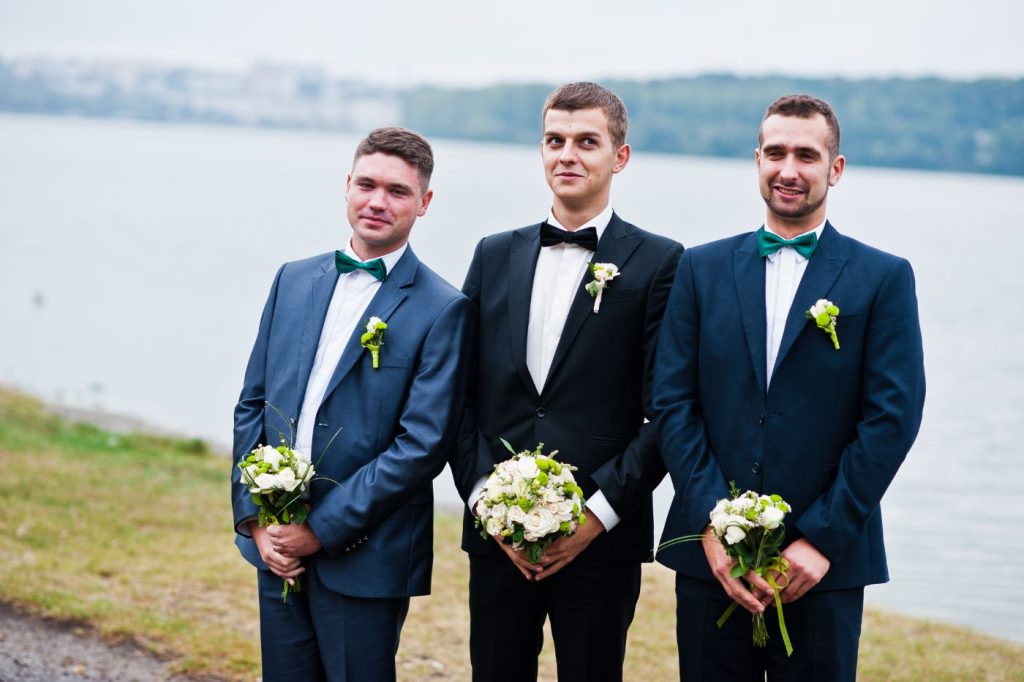 groom and two groomsmen holding bouquets