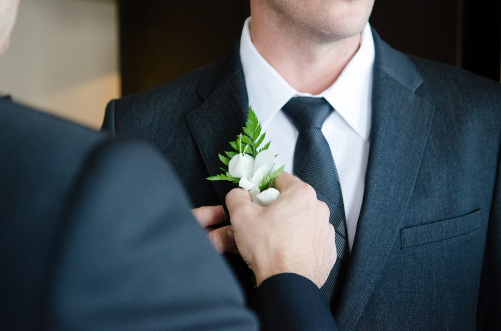 man attaching a boutonniere on the groom's suit