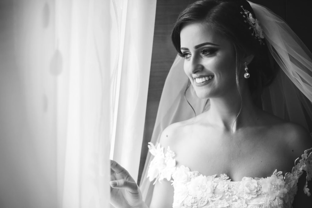 smiling bride in wedding attire looking out a window