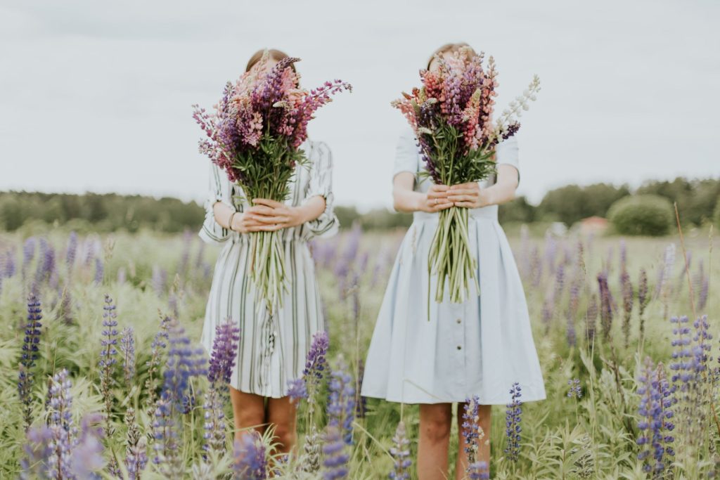 women wearing dresses standing in a field holding a bunch of flowers