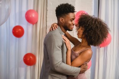 African American couple hugging and dancing near balloons in apartment